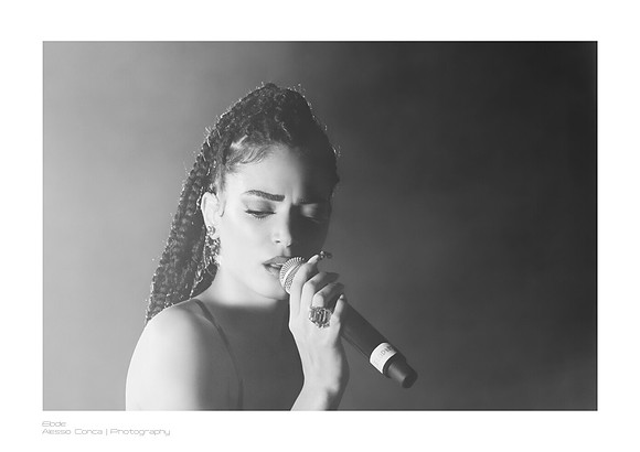 Black-and-white photograph of Elodie in concert at the Circolo Magnolia in Segrate; a close-up of the artist with half her face illuminated and half in shadow, in a fine art chiaroscuro style.