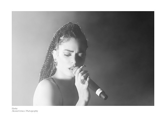 Black-and-white photograph of Elodie in concert at the Circolo Magnolia in Segrate; a close-up of the artist with half her face illuminated and half in shadow, in a fine art chiaroscuro style.