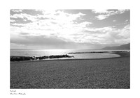 Artistic black-and-white photograph of the beach at Ventimiglia in Liguria, featuring rocks, cliffs, and a contrasting cloudy sky.